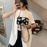 A woman holding a mini suitcase bag. The bag has a shoulder strap and appears to be black with a white polka dot pattern, featuring a cross-body design and possibly multiple compartments or pockets