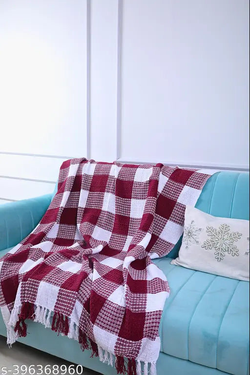 A red and white plaid throw blanket with fringed ends draped over the back of a two-seater sofa