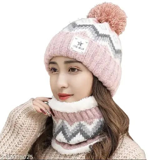 The image shows a beige scarf with a pink pom-pom, worn around the neck and paired with a matching knitted hat that features a pom-pom on top. The scarf appears to be made of a wool material, suitable for cold weather activities like skiing or hiking