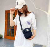 A woman wearing a white t-shirt with a baseball cap on her head, smiling at the camera. She has a navy blue shoulder bag with a daisy design and yellow straps