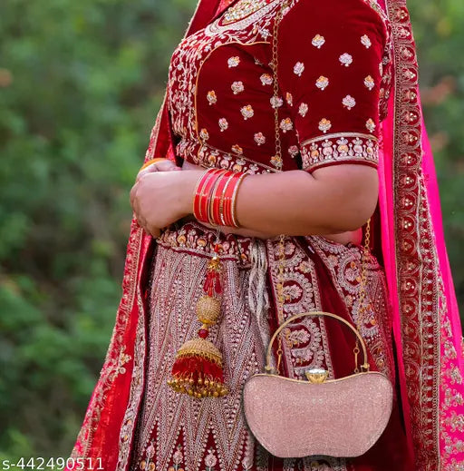 The image displays an elegant handcrafted evening clutch bag with a pink resin finish. It's a stylish partywear accessory, likely for women, with an apple-shaped design that features a flap closure. The handbag is adorned with tassels and has a spacious interior compartment suitable for holding essentials