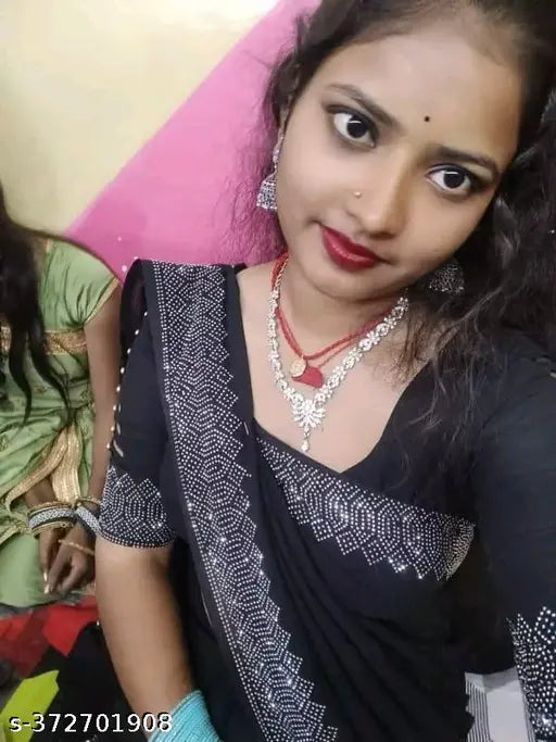 A woman posing with a smartphone in a black and white saree, adorned with red jewelry