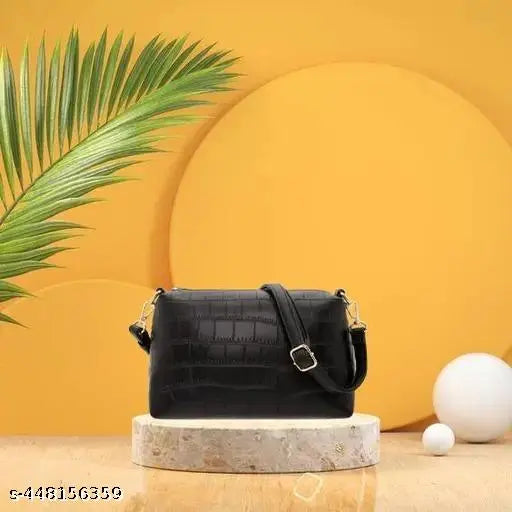 Trendy women's handbag with leather construction. Black color, likely made of faux leather or a similar material, featuring what seems to be a simple yet elegant design with silver-toned hardware and a single shoulder strap. The bag appears to be in a casual setting on a table, possibly for display purposes