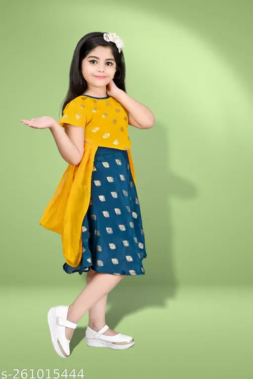 A woman in a yellow sari with blue polka dots, standing against a green backdrop