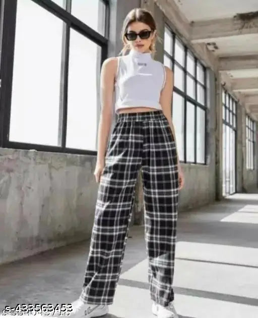 Woman in plaid trousers with white top, black sunglasses, standing outside near a wall