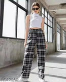 Woman in plaid trousers with white top, black sunglasses, standing outside near a wall