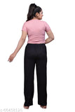 Woman in black pants with white dots, black sleeveless top, standing against a plain background