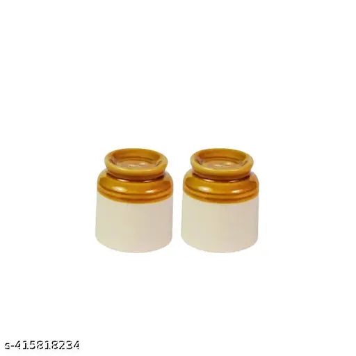 The image displays a pair of cylindrical ceramic containers with metal lids, each containing what appears to be granular salt or pepper. These containers are white and have a textured surface. They are labeled as "Ceramic Martban 4000 kg" and "Achaar Barni." One container is slightly off-center in the image