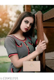 A woman leaning against a wooden fence, wearing a black and white polka dot dress with red accents, holding up her hair