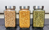 Trendy glass jars with lids, containing different colored spices or grains, set of three