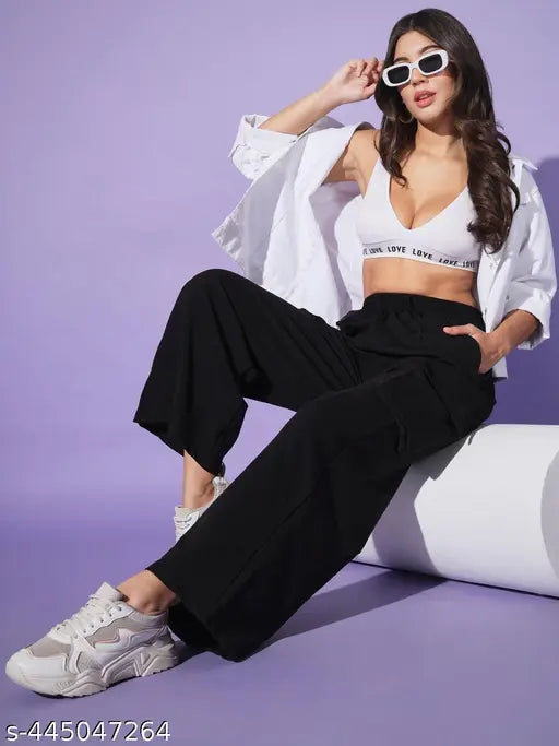 Woman wearing black pants, white jacket with cutouts, and sunglasses, posing against a purple background