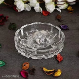 The crystal plate is empty and features a turtle motif on top. It sits against a gray surface, surrounded by small, colorful leaves or petals