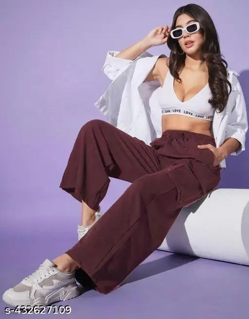A woman in a white crop top, brown high-waisted pants, and silver sneakers