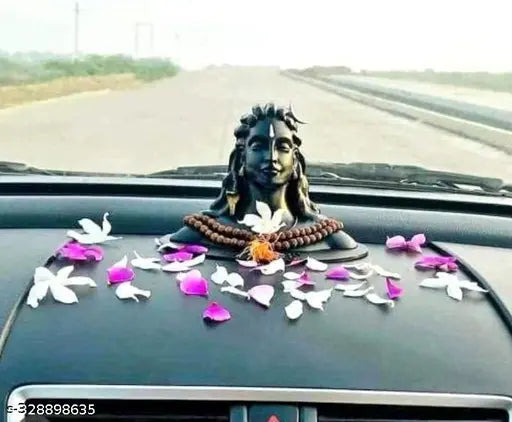 A car's dashboard adorned with a religious Rudraksha, a statue of Lord Adiyogi Shankara, and petals in shades of pink and white