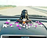 A car's dashboard adorned with a religious Rudraksha, a statue of Lord Adiyogi Shankara, and petals in shades of pink and white
