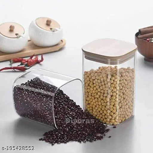 Square glass jar with wooden lid, containing brown dry fruit, next to another similarly styled jar. One jar is larger and the other is smaller. Jars appear airtight with visible rust-proof bamboo wood lids