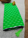 Green and black leheriya saree with fringe detail, in a coiled form on table