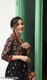 A woman in a patterned dress, smiling and holding her hair