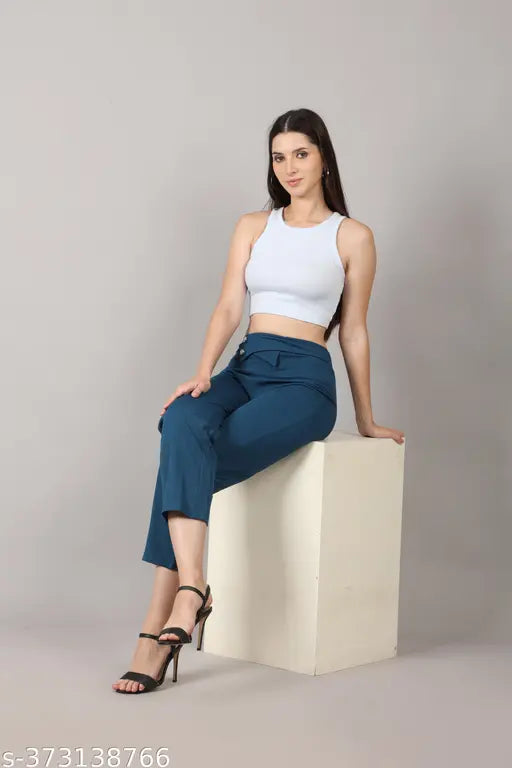 A person is sitting on a white stool, wearing high rise trousers in a navy blue color. The trousers appear to be of fashionable design and are part of the PA CREATION collection for women and girls