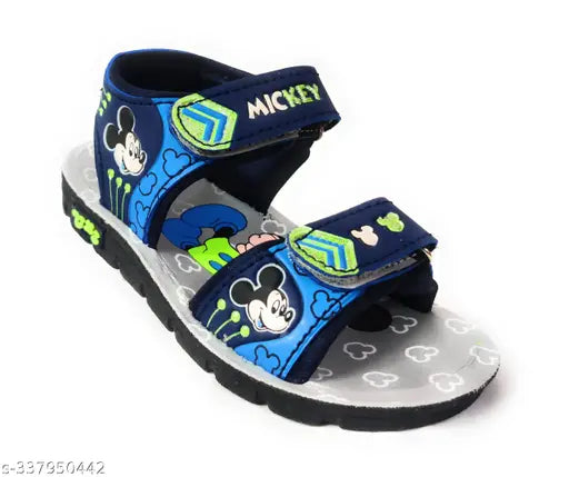 This image depicts a pair of fashionable casual sandals designed for children. The sandals are predominantly black with blue and green accents. Each sandal features a playful Minnie Mouse design, complete with her signature polka-dot bow. A unique element is the inclusion of a small cartoon character on the strap. The straps themselves have a fun cartoon print in shades of blue and green, complementing the color scheme of the sandals
