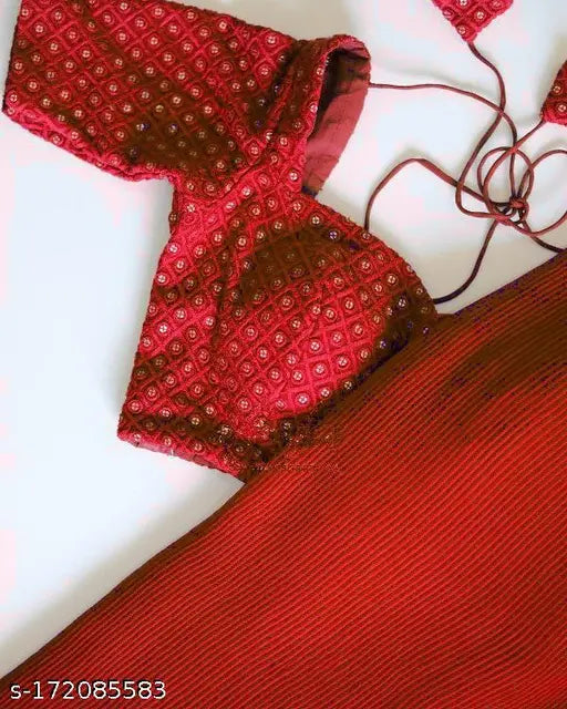 The image is a photograph of a red paisley print saree with a matching blouse draped over it. The blouse features thin, off-the-shoulder straps and appears to be unbuttoned or unzipped in the front, revealing a partial glimpse of an interior top layer beneath. The saree is hanging flat against a white background