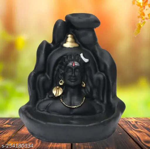 Black, ceramic figurine of a Hindu deity with jewelry, sitting in an ornate holder against a blurred autumnal background
