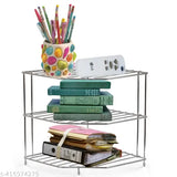 This is a silver 3-tier shelf, organized with various items. On the top shelf, there are two cups of colorful writing instruments and a smartphone in a white case. The middle shelf holds three books, while the bottom shelf contains what appears to be binders and possibly some papers. The shelf is set against a backdrop of other household goods