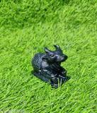 Black stone sculpture depicting a cow sitting on grass