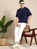 A man wearing a white jean with rolled-up cuffs, a navy blue shirt, and sunglasses. He's posing in front of a potted plant against a light-colored wall
