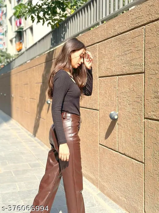 Brown leather trousers on a woman in an urban setting, standing by a brick wall