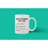 The image depicts a white ceramic coffee mug with printed text. The mug is round and has a comfortable handle on its side. The printed text on the mug reads "HOW TO DRINK HOT TEA" in black letters, followed by instructions on making tea, emphasizing the use of honey instead of sugar. Additionally, there's a statement about not being too hot with a warning that too much tea can be harmful