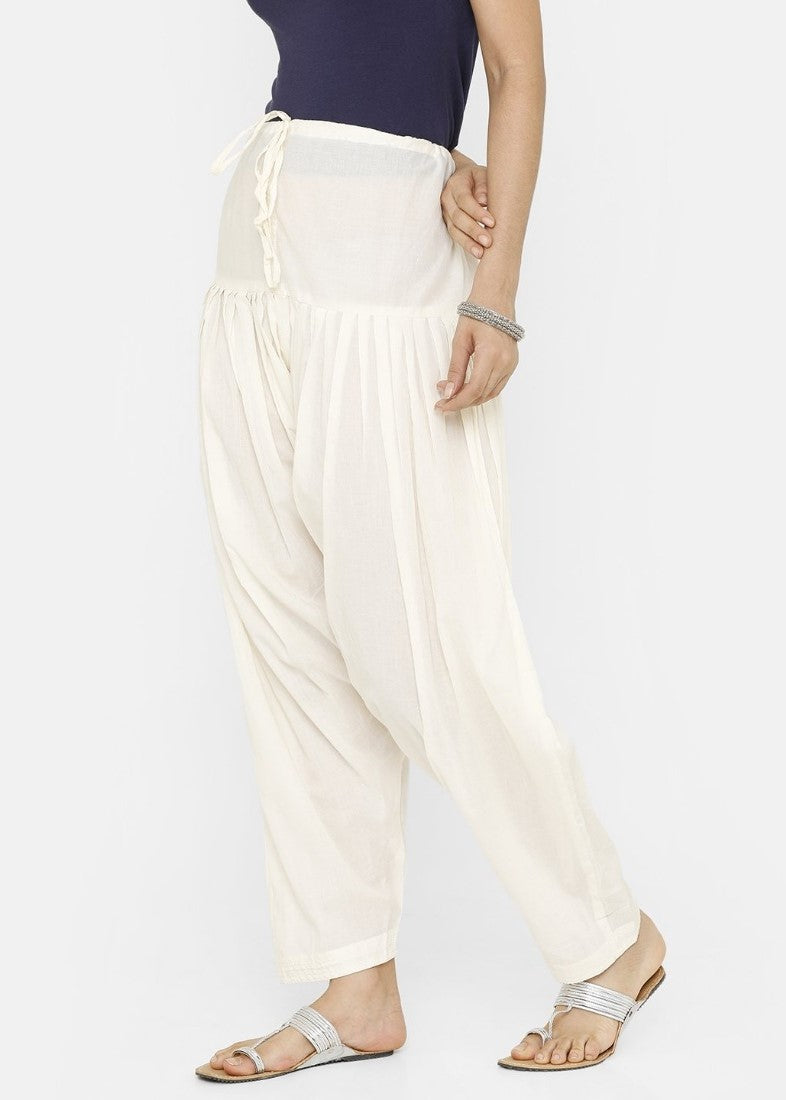 Woman wearing a long white tunic with a high waist and an elastic waistband, paired with wide-leg cream pants